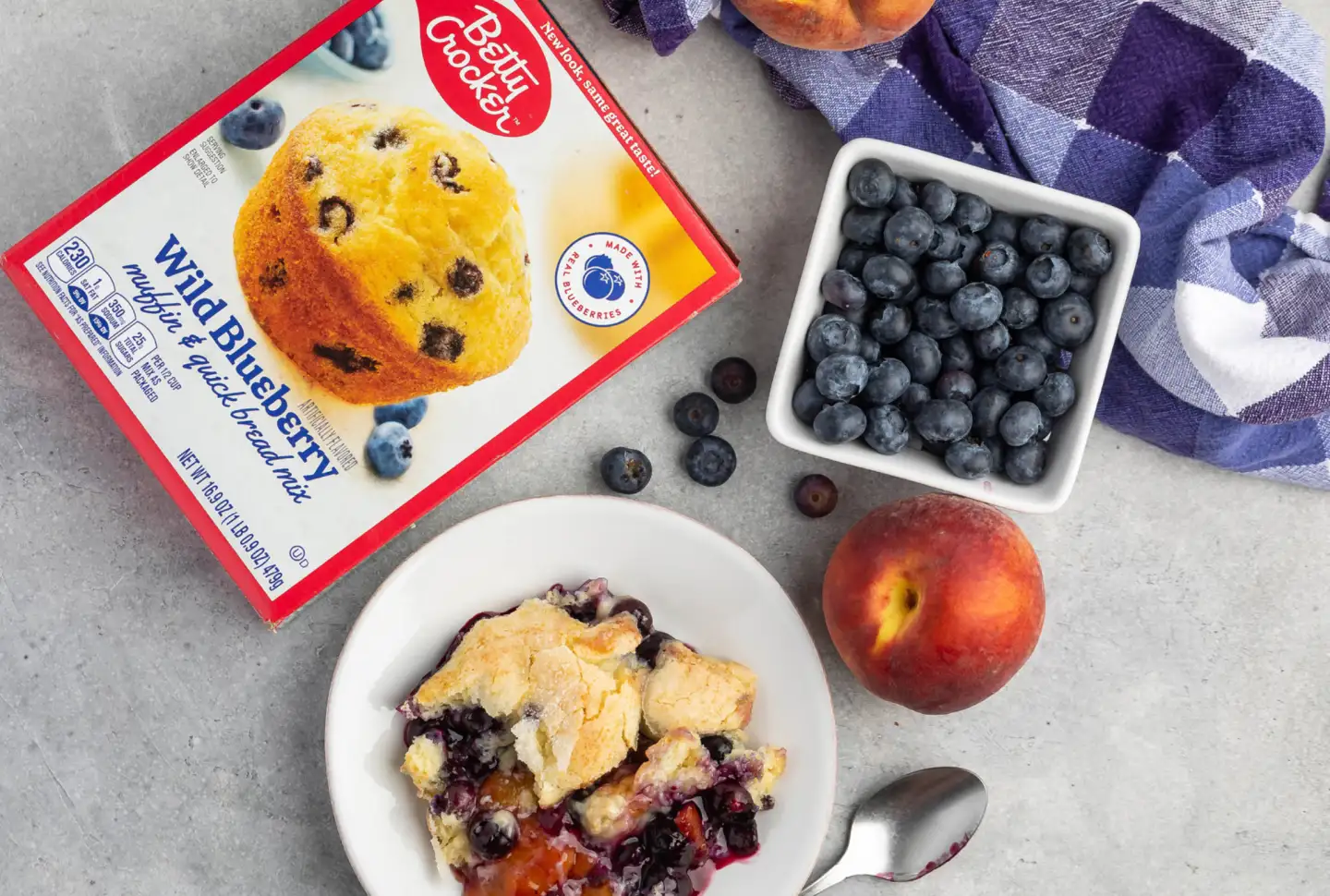 A serving of wild blueberry peach cobbler in a bowl alongside a box of Better Crocker muffin mix