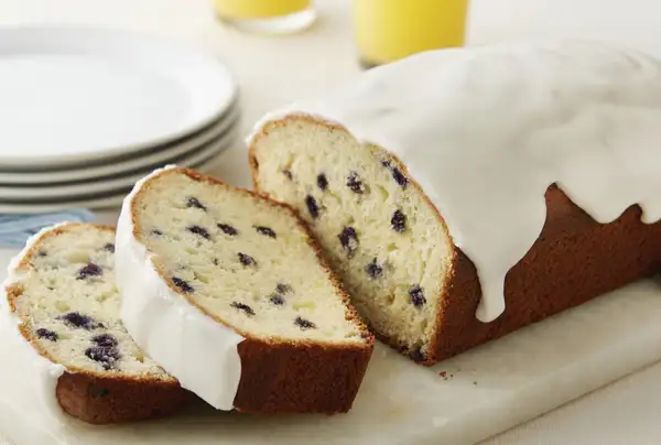 A cutting board of sliced lemon wild blueberry bread with icing